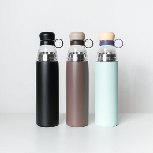 Three reusable insulated water bottles standing upright on a white shelf against a light gray wall. The bottles have matte black, taupe-brown, and pale mint-green bodies with clear upper sections and loop handles.