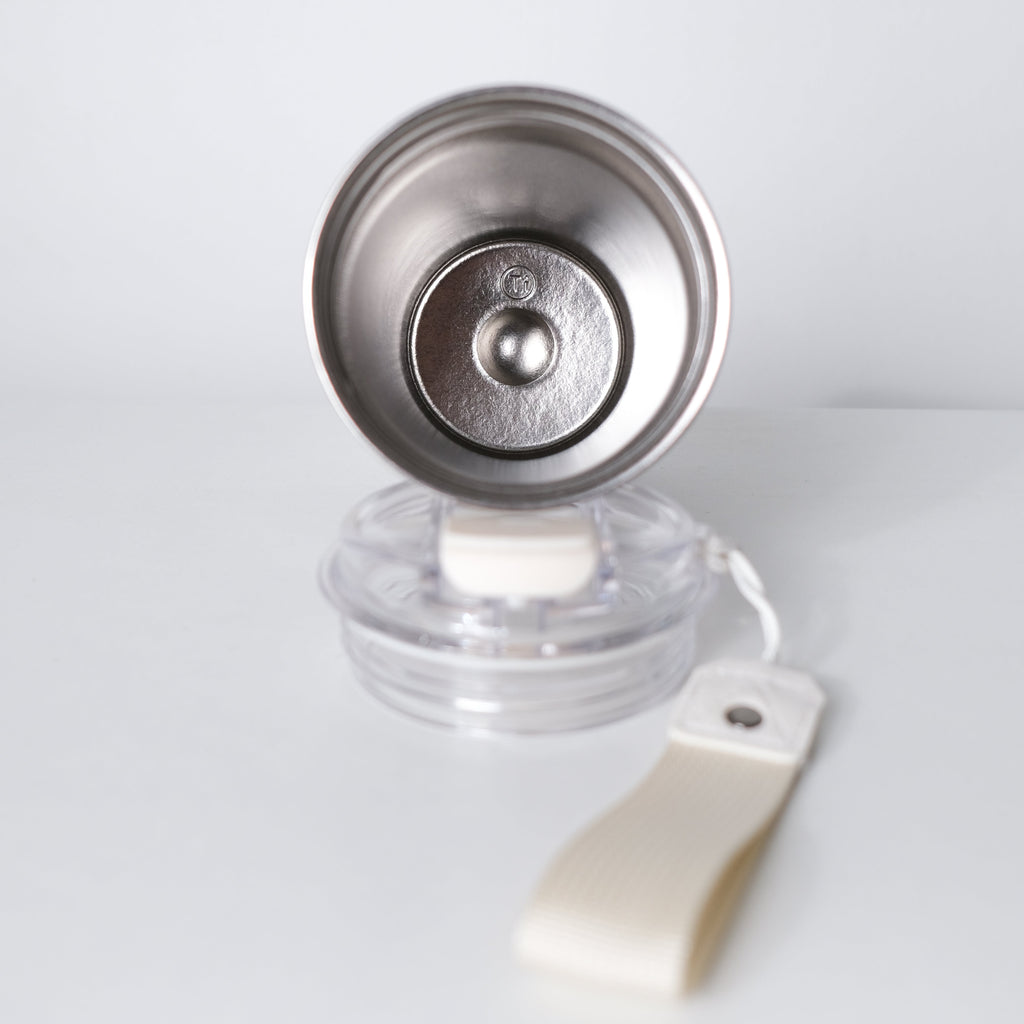 A stainless steel coffee pour-over dripper with a clear plastic base and an off-white fabric loop, photographed on a clean white background.